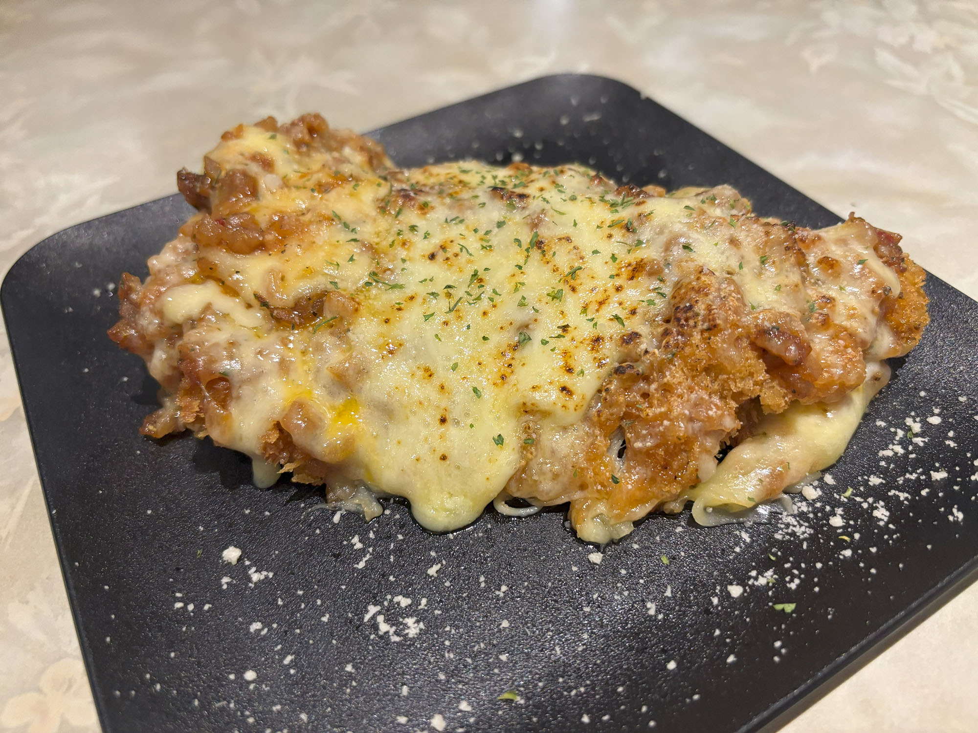 【 チキンパルミジャーノ 】（660円）
チーズ好きには絶対食べてほしいチキンパルミジャーノ。
サクサクに揚げたチキンの上には、とろ〜り伸びるチーズがたっぷり。ナイフを入れると、衣のカリッとした音がして、中のお肉はめちゃくちゃジューシー！チーズの濃厚さとお肉の旨みが相性抜群で、ついもう一口食べたくなるおいしさ。
